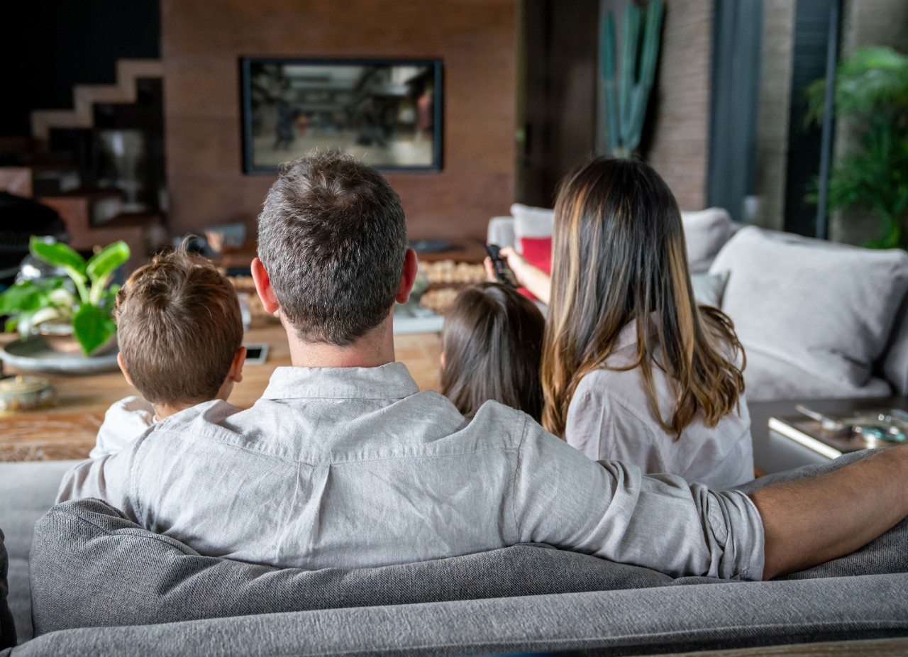 Backview of latin american family at home watching TV while mom changes channels