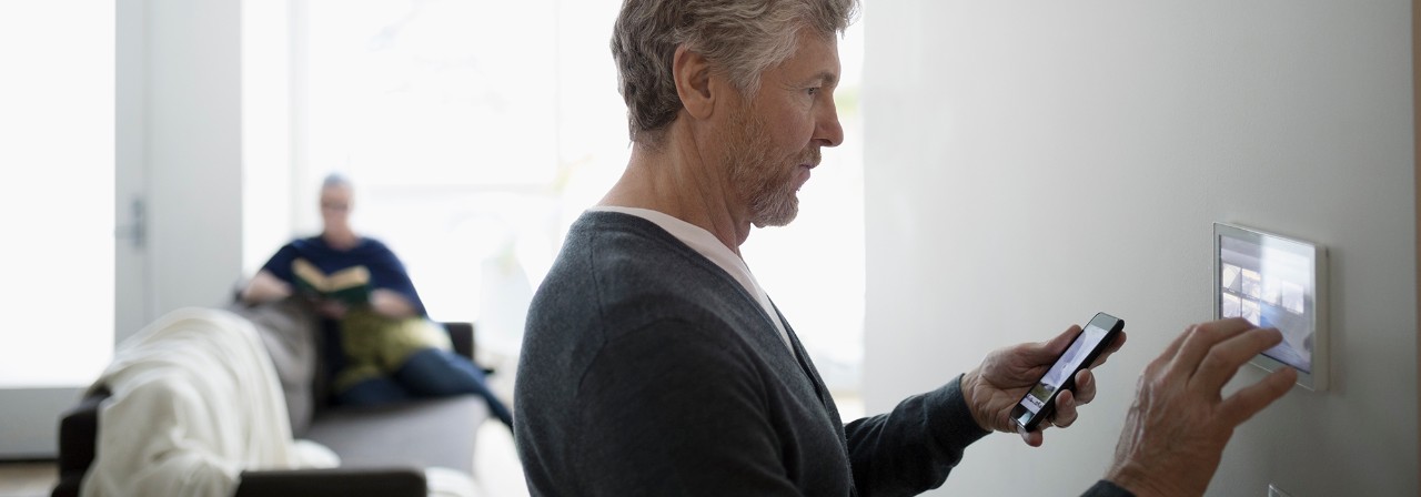 Man syncing his connected home devices - smartphone to smart wall panel. 