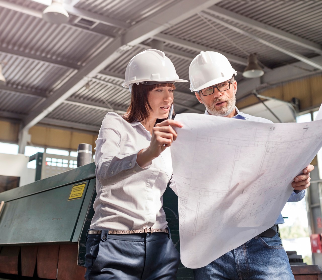 Man and woman engineer wearing white hardhats looking at blueprints. 