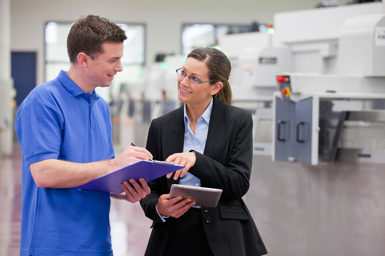 Smiling technician and businesswoman with clipboard and tablet in hi-tech manufacturing plant