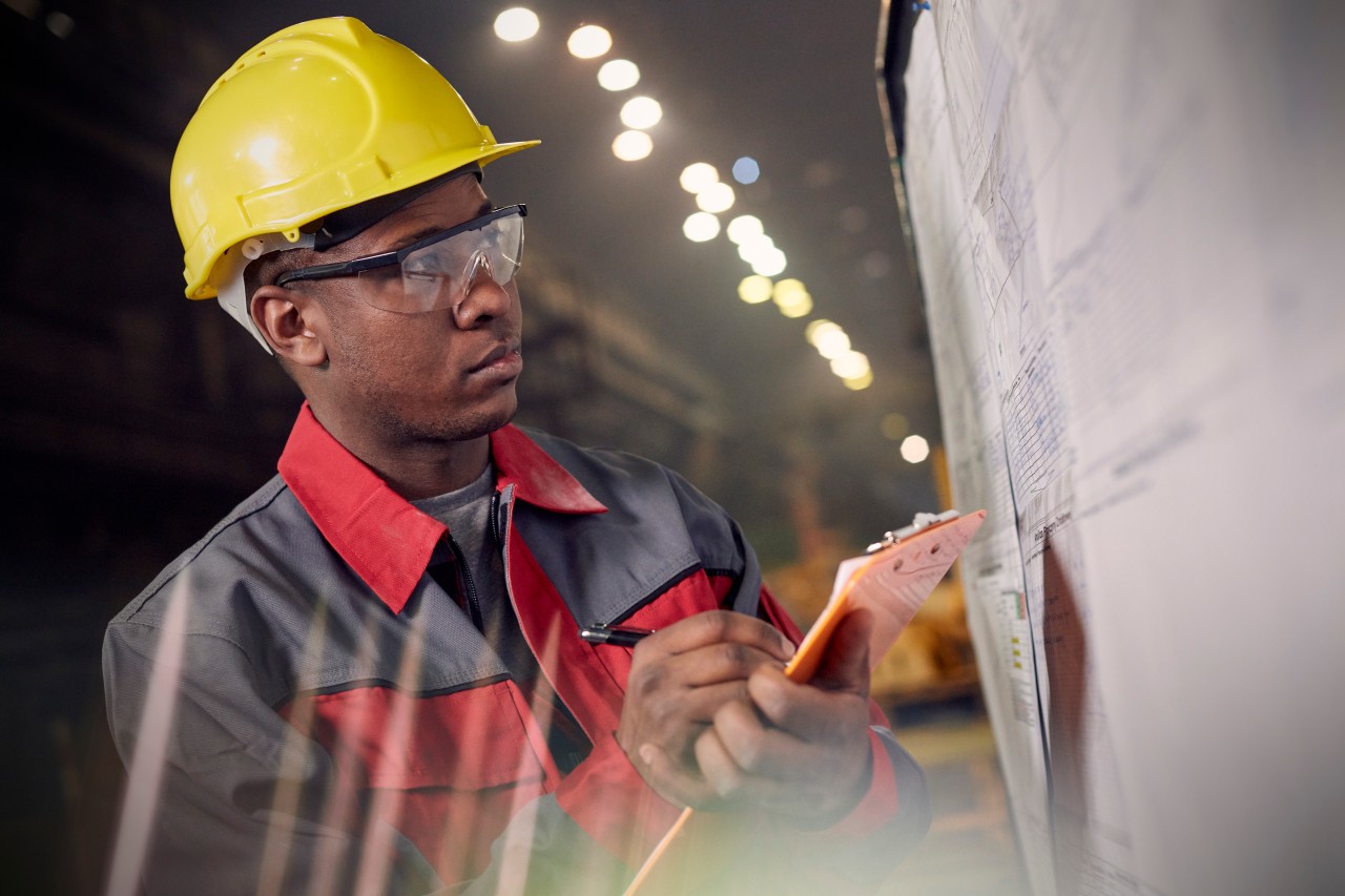 Focused steelworker with clipboard at information board in steel mill