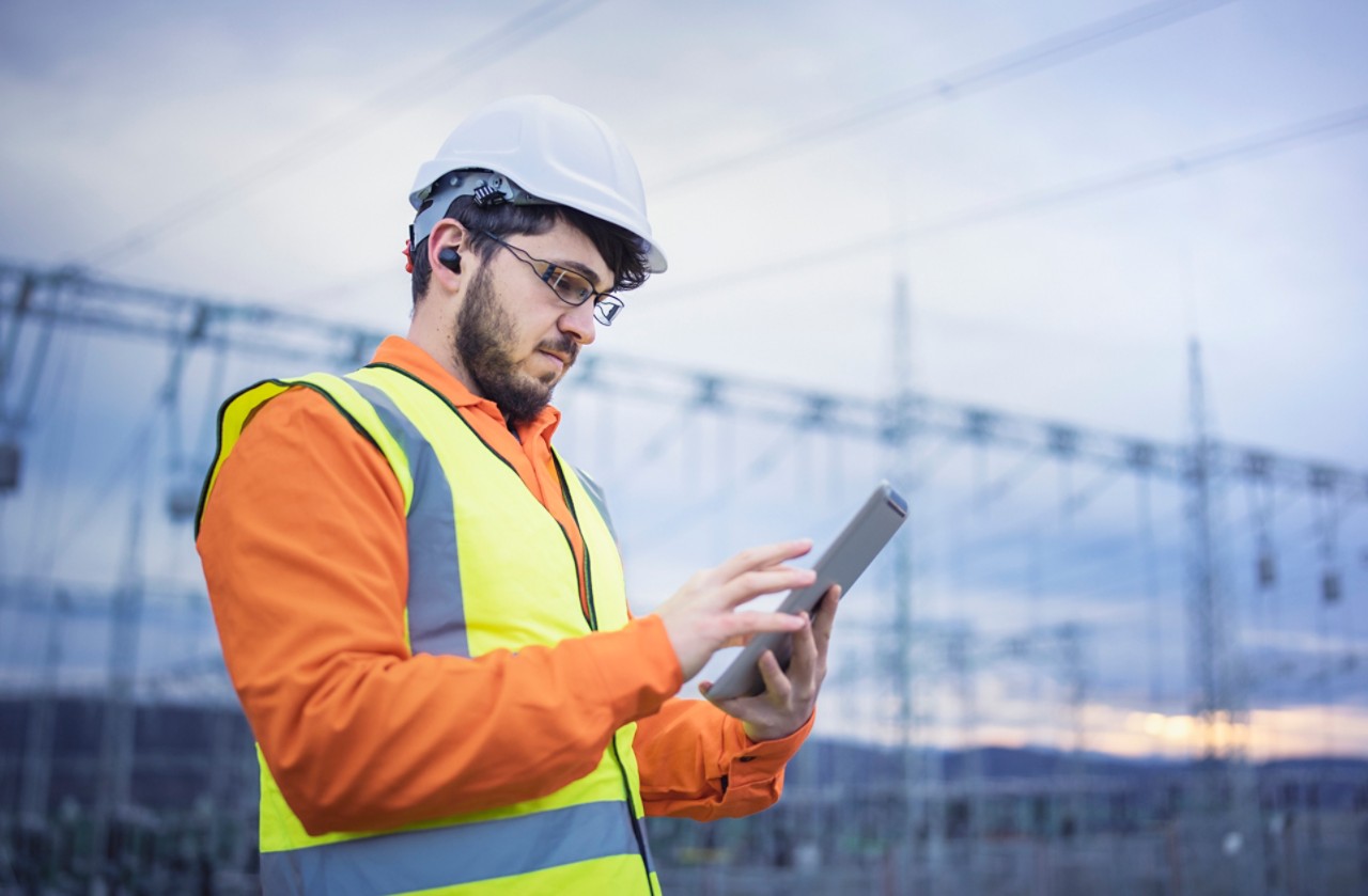 A shot of an electrical engineer using a digital tablet and hands-free device while working in power substation.